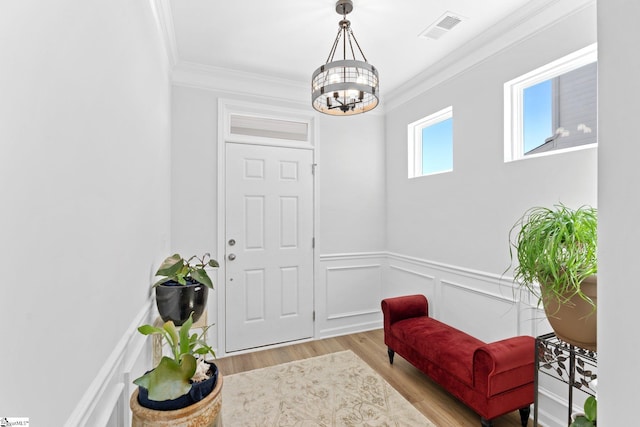 interior space with visible vents, a wainscoted wall, wood finished floors, an inviting chandelier, and crown molding