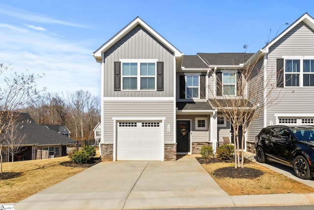 view of front of house with a garage, driveway, stone siding, fence, and board and batten siding