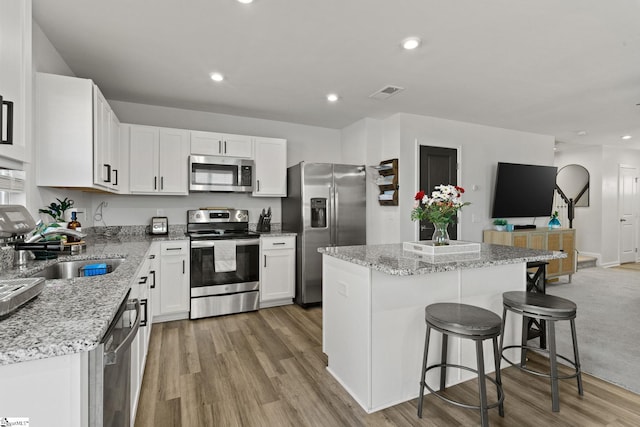 kitchen with white cabinets, appliances with stainless steel finishes, a center island, light wood-type flooring, and a sink