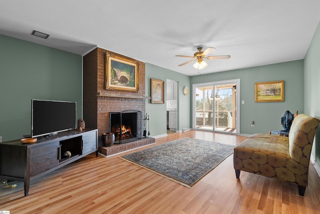 living room with a ceiling fan, a brick fireplace, baseboards, and wood finished floors