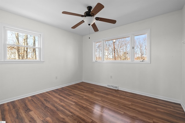 spare room with dark wood-style flooring, visible vents, plenty of natural light, and baseboards