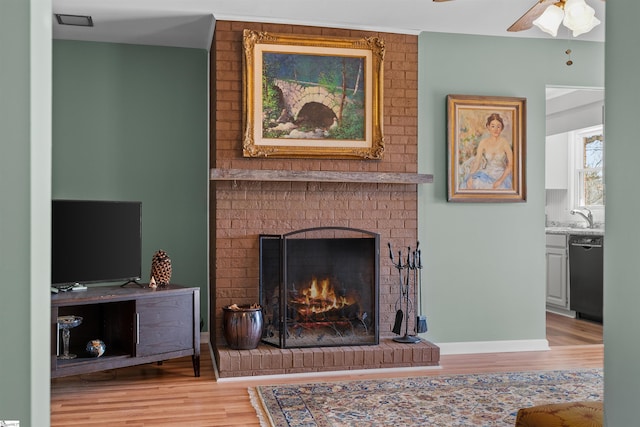 living area with light wood finished floors, a fireplace, a ceiling fan, and baseboards