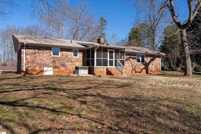 back of house featuring a sunroom, a chimney, a yard, central air condition unit, and brick siding