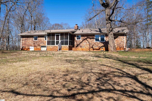 back of house featuring brick siding, a sunroom, a lawn, crawl space, and a chimney