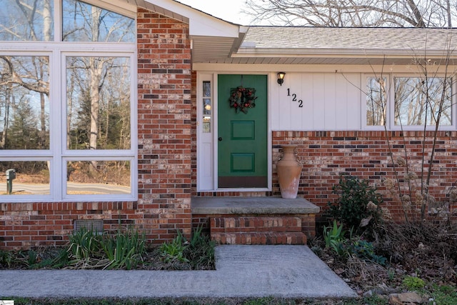 doorway to property with brick siding and roof with shingles