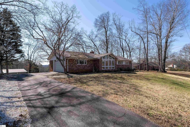 view of front of home with aphalt driveway, a front lawn, a chimney, and a garage