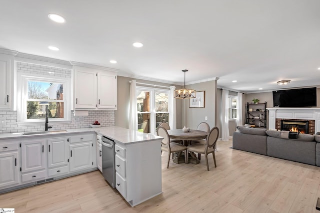 kitchen featuring dishwasher, a peninsula, a sink, and light wood-style flooring