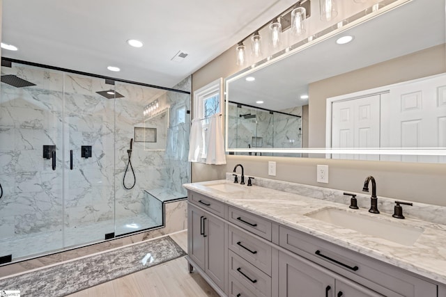 bathroom with visible vents, a sink, a marble finish shower, and wood finished floors