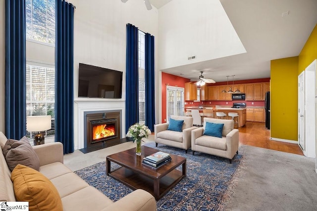 living room with ceiling fan, visible vents, a fireplace with flush hearth, and a towering ceiling