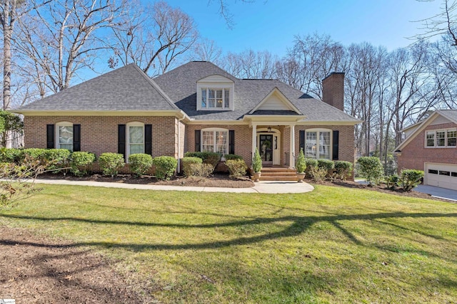 view of front of property with a shingled roof, a front yard, a chimney, and brick siding