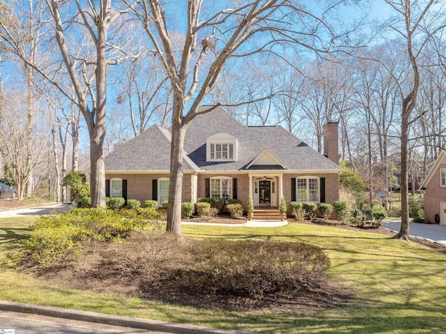 view of front of property featuring a shingled roof, a front lawn, and brick siding