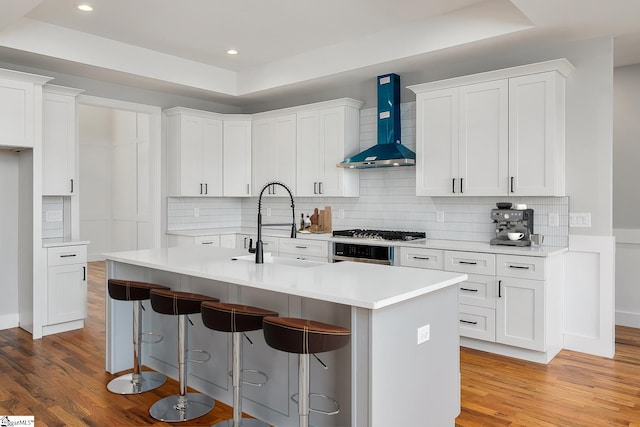 kitchen with wall chimney range hood, a kitchen bar, light wood finished floors, and a sink