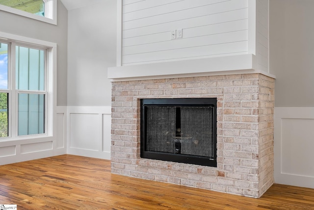 interior details featuring a brick fireplace, a decorative wall, wood finished floors, and a wainscoted wall