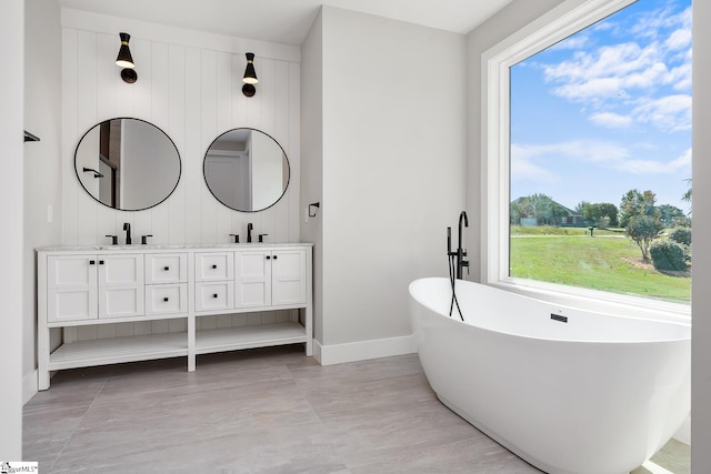 bathroom featuring a freestanding bath, double vanity, a sink, and baseboards