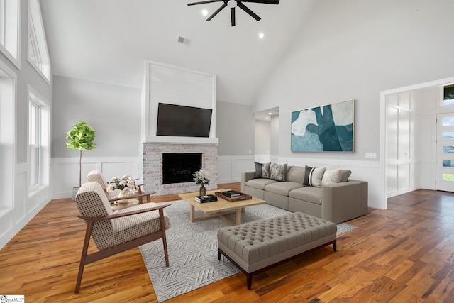 living room featuring high vaulted ceiling, a wainscoted wall, a fireplace, visible vents, and light wood-type flooring