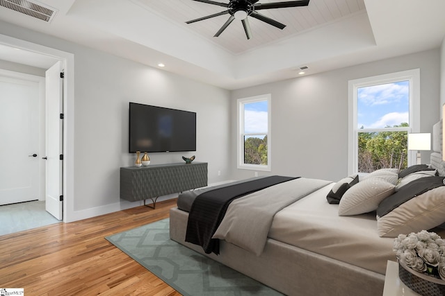 bedroom featuring a tray ceiling, multiple windows, visible vents, and light wood-style floors