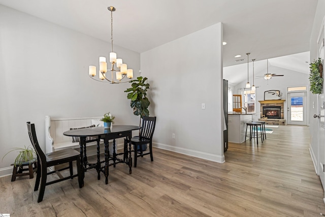 dining room with a fireplace, lofted ceiling, wood finished floors, baseboards, and ceiling fan with notable chandelier