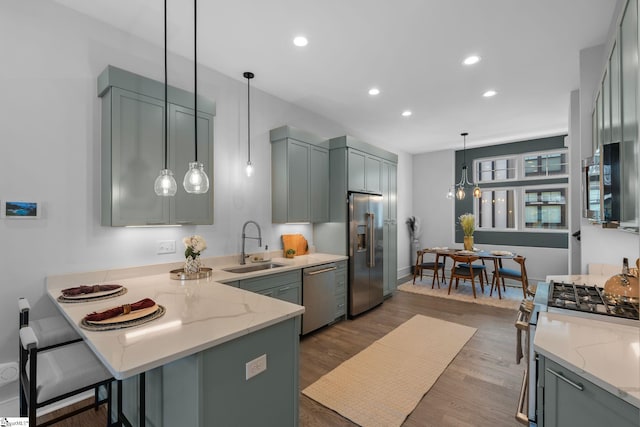 kitchen with a peninsula, appliances with stainless steel finishes, a sink, and light stone countertops