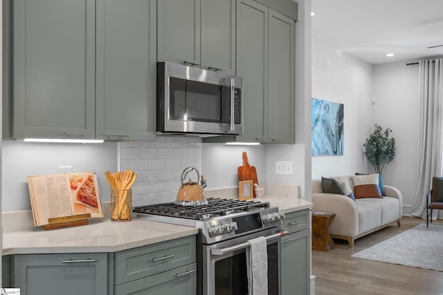 kitchen with light wood finished floors, appliances with stainless steel finishes, backsplash, and gray cabinetry