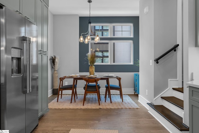 dining area with dark wood-type flooring, stairway, an inviting chandelier, and baseboards