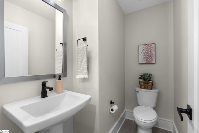 half bath featuring baseboards, a sink, and toilet