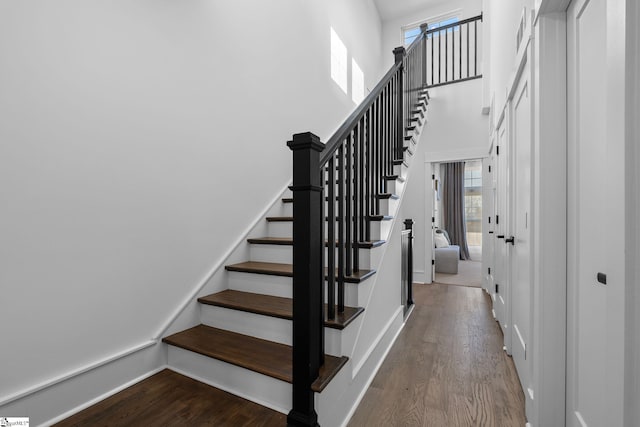 stairway featuring wood finished floors, a towering ceiling, and baseboards