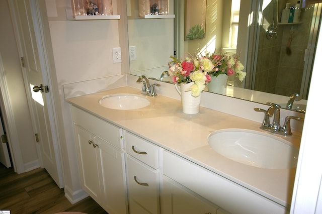 full bath featuring wood finished floors, double vanity, tiled shower, and a sink