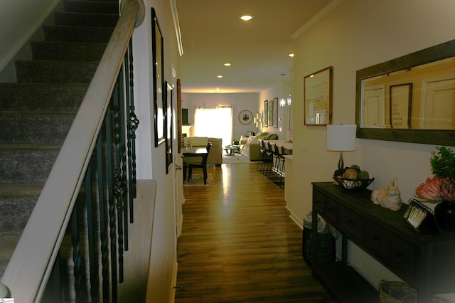 corridor with dark wood-type flooring, recessed lighting, ornamental molding, and stairs