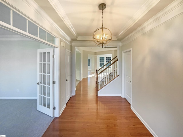 corridor with a notable chandelier, ornamental molding, wood finished floors, baseboards, and stairs