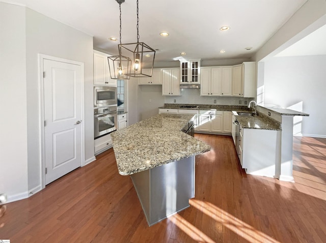 kitchen featuring stainless steel appliances, dark wood-style flooring, a sink, backsplash, and dark stone counters