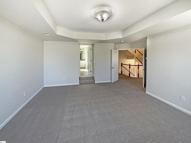 carpeted empty room featuring stairway and baseboards