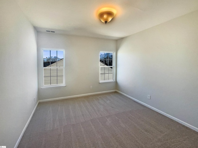 carpeted empty room with a healthy amount of sunlight, visible vents, and baseboards