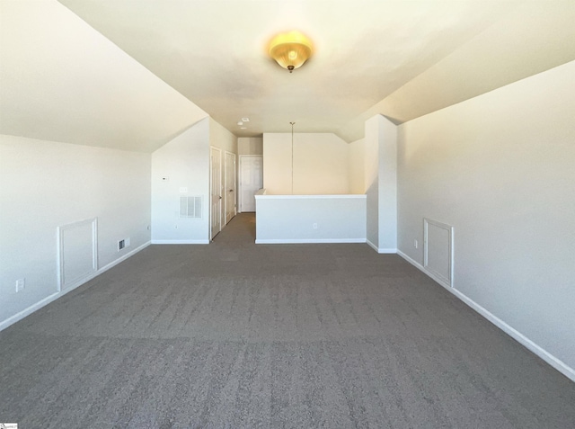 additional living space featuring lofted ceiling, dark carpet, visible vents, and baseboards