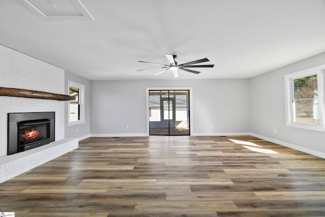 unfurnished living room with a wealth of natural light, a fireplace, baseboards, and wood finished floors