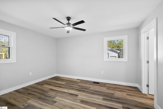 empty room featuring a ceiling fan, visible vents, baseboards, and wood finished floors