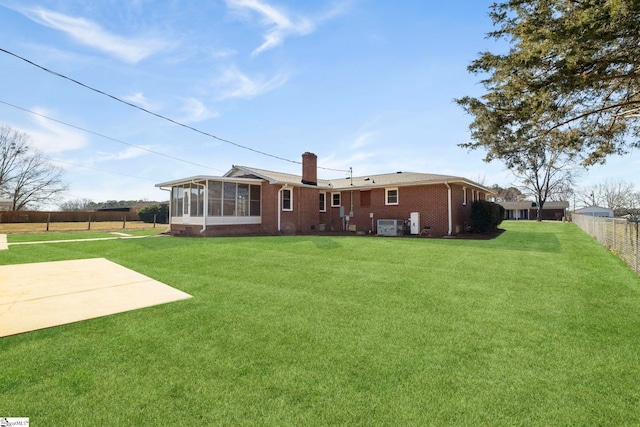 rear view of house with brick siding, fence, a sunroom, a lawn, and a chimney