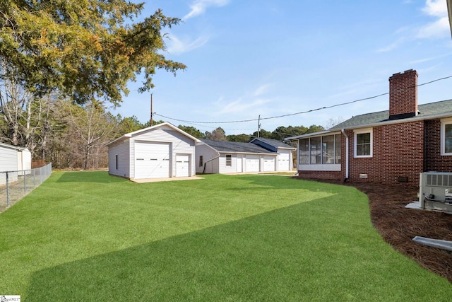 view of yard featuring a garage, a sunroom, fence, and an outbuilding