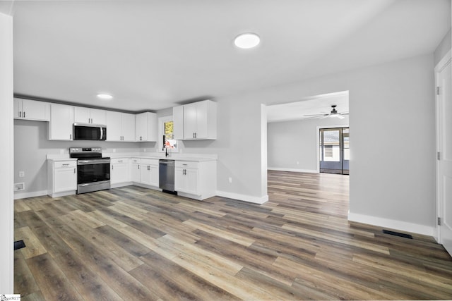 kitchen with dark wood-style floors, stainless steel appliances, light countertops, white cabinetry, and baseboards