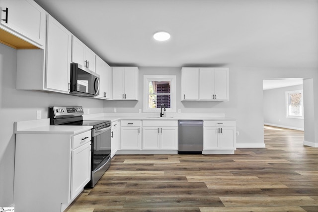 kitchen with appliances with stainless steel finishes, white cabinets, a sink, and wood finished floors