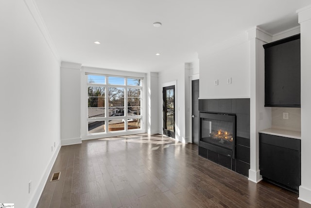 unfurnished living room with crown molding, dark wood finished floors, visible vents, a tile fireplace, and baseboards