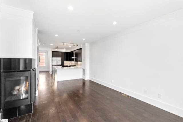 unfurnished living room featuring dark wood-style floors, recessed lighting, ornamental molding, a lit fireplace, and baseboards