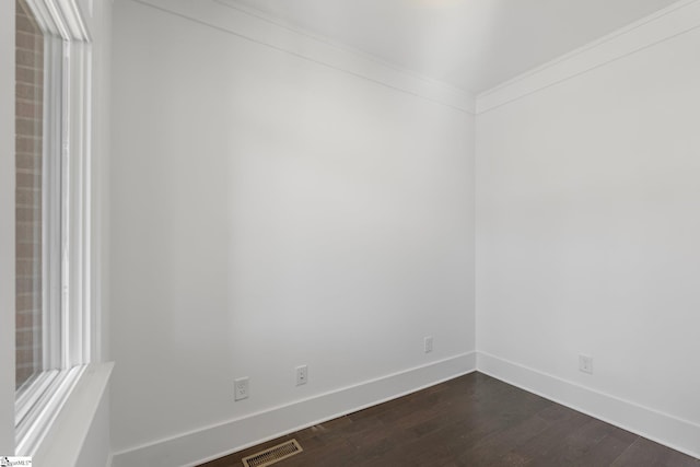 empty room with baseboards, visible vents, dark wood-type flooring, and ornamental molding