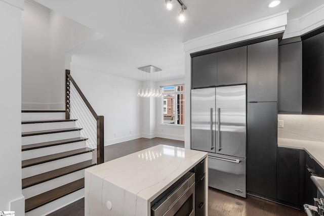 kitchen with dark wood-type flooring, a kitchen island, light stone countertops, dark cabinets, and built in appliances