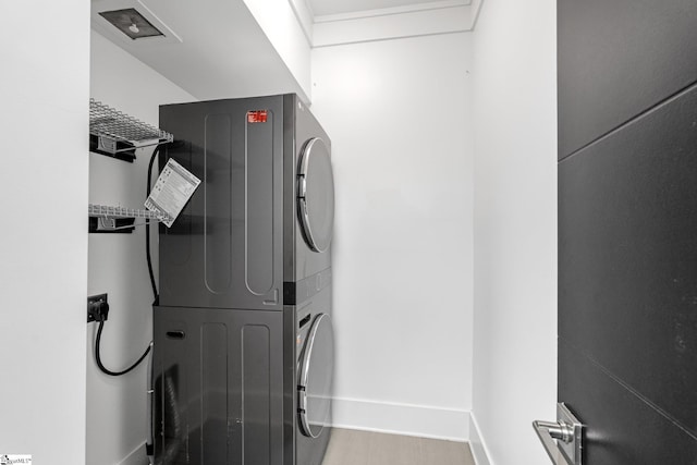 clothes washing area with laundry area, stacked washing maching and dryer, baseboards, and wood finished floors