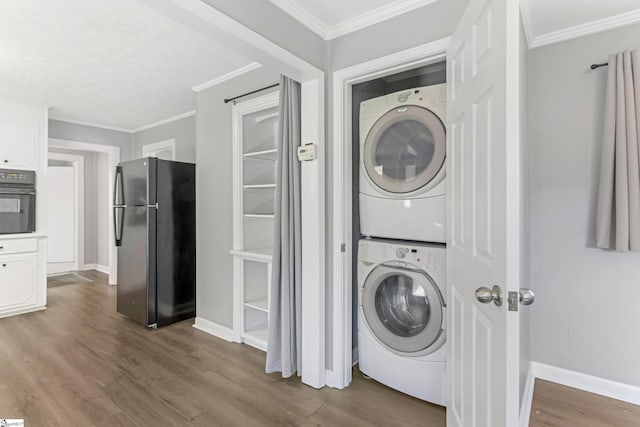 laundry room featuring laundry area, baseboards, stacked washer / drying machine, wood finished floors, and crown molding