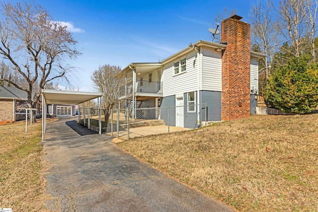 view of front facade featuring driveway, a chimney, fence, a front lawn, and a carport