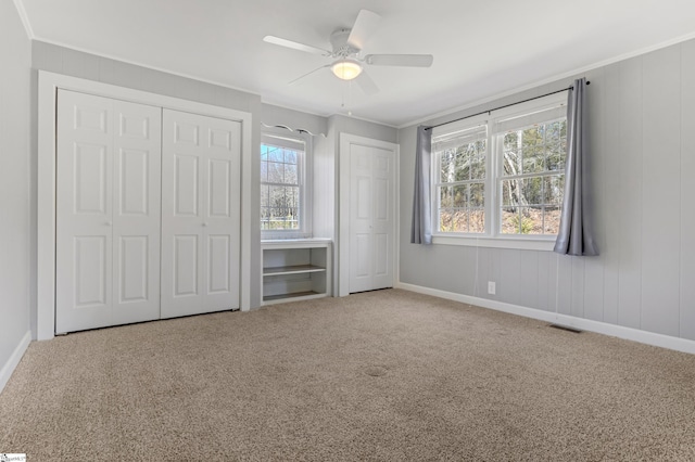 unfurnished bedroom featuring crown molding, multiple windows, carpet, and multiple closets