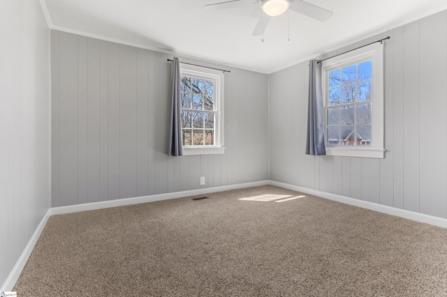 carpeted spare room featuring ornamental molding, a wealth of natural light, baseboards, and a ceiling fan