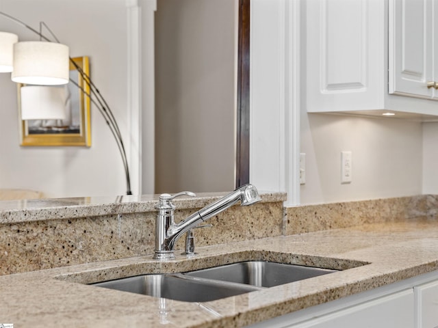 room details with light stone counters, white cabinetry, a sink, and hanging light fixtures