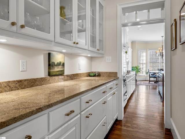 bar with baseboards, dark wood-type flooring, an inviting chandelier, and crown molding